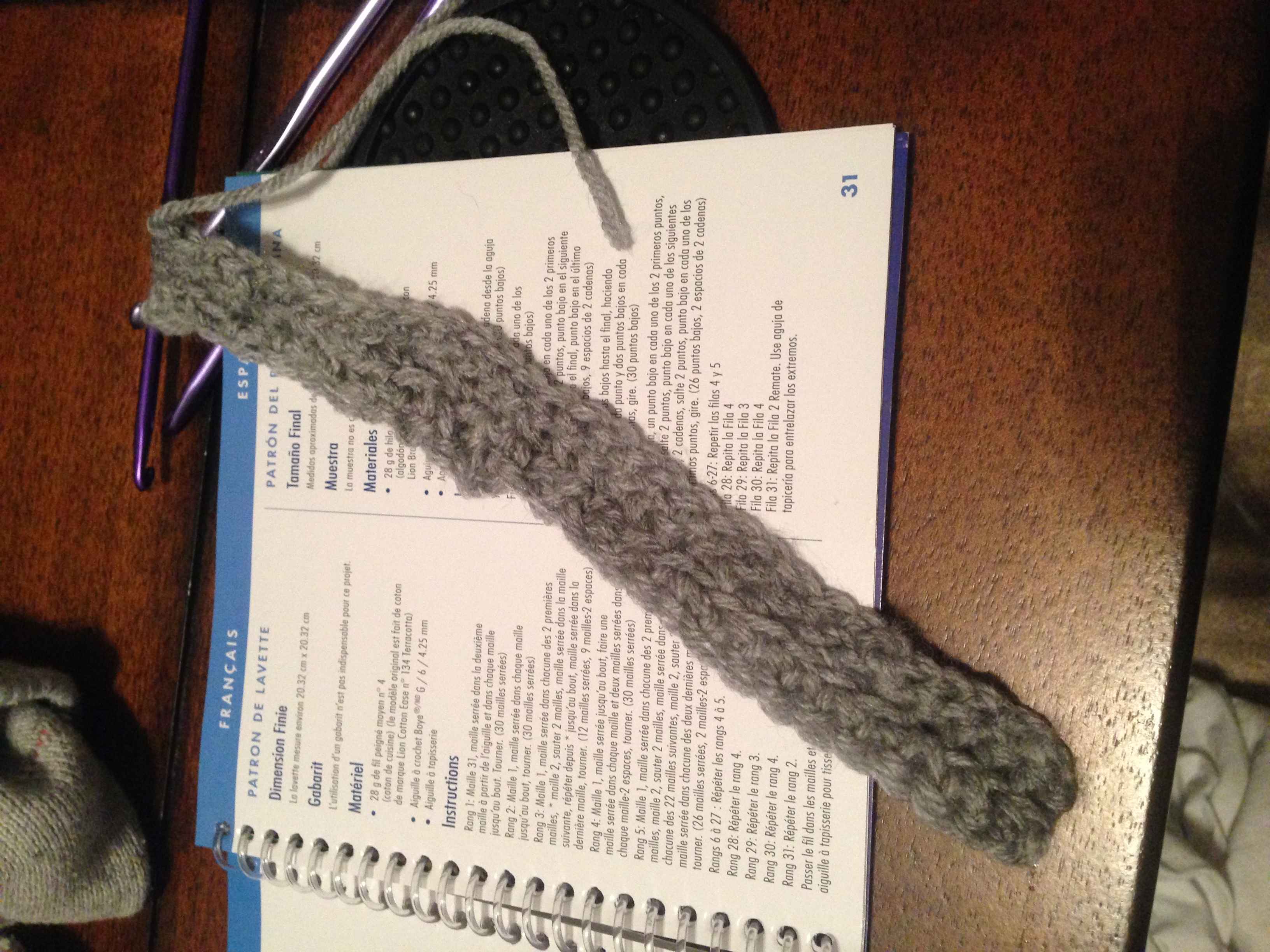 Foot long swatch of grey yarn laying on a book of How to Crochet instructions