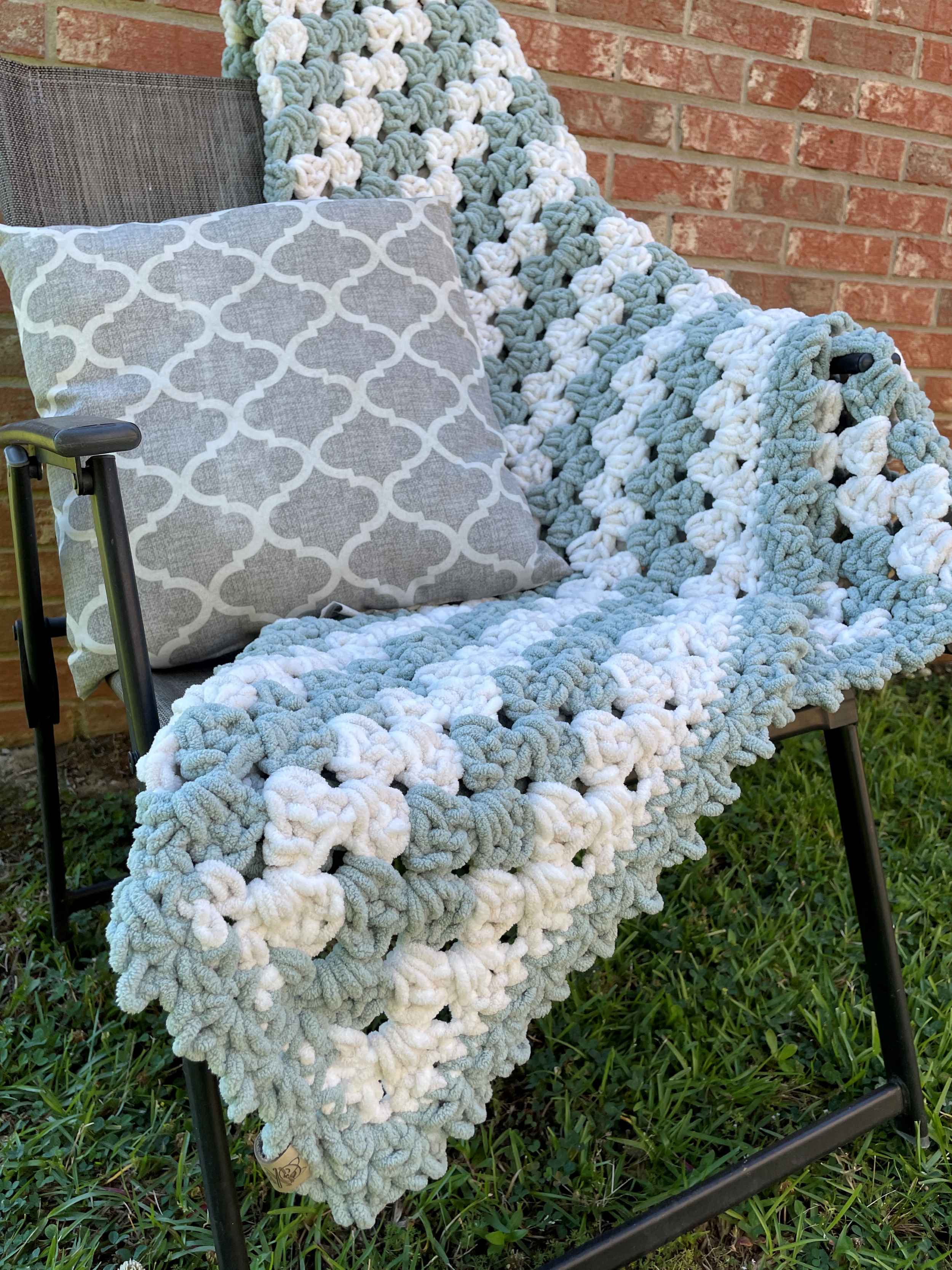 Speedy Granny Stripe Blanket in stripes of Misty Green and Beach Foam with a Misty Green Border sitting on a chair with a pillow